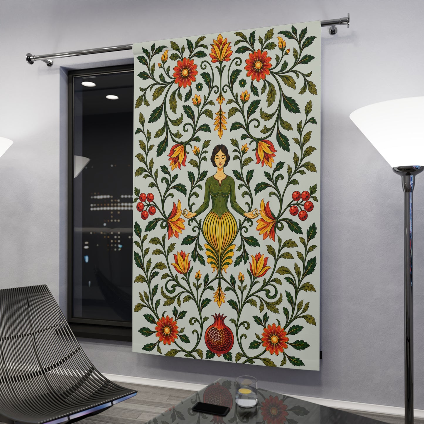 A large fabric wall hanging or tapestry displayed in a modern room. The tapestry features a folk-art style design with a central female figure surrounded by symmetrical floral and vine motifs in green, red, orange, and yellow on a light background.