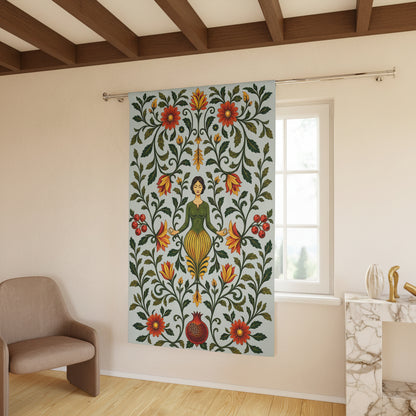 A tall window curtain panel hanging in a bright room, featuring a folk-art style design of a woman surrounded by green vines and red, orange, and yellow flowers on a pale blue background.