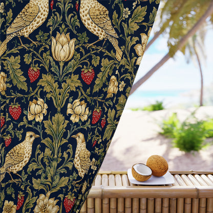 A close-up of a dark navy velvet curtain featuring a classic William Morris-style floral and bird pattern in gold, beige, and red, shown hanging next to a bamboo table with coconuts in a tropical beach setting.